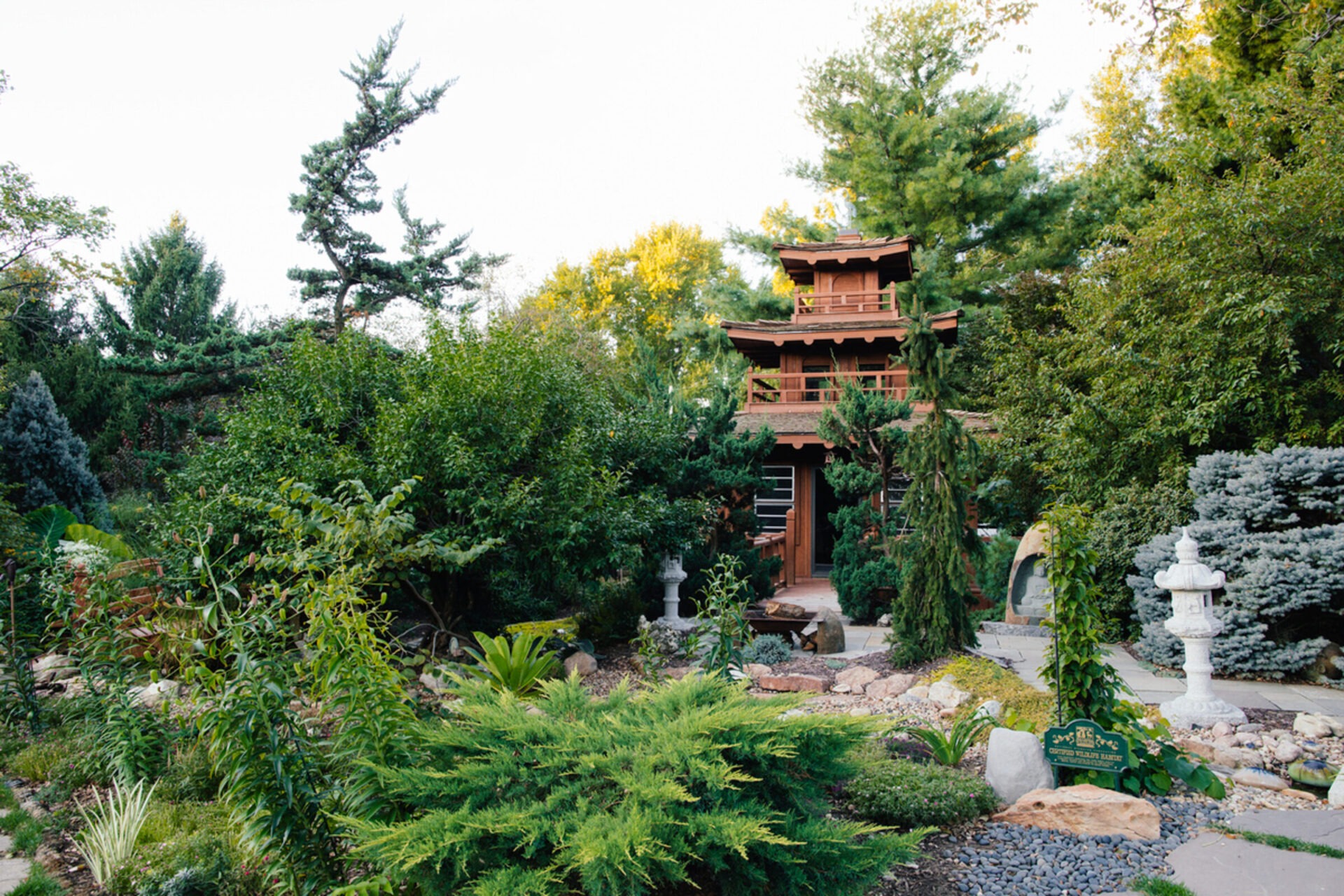 Traditional Japanese garden with lush greenery, stone lanterns, and a wooden pagoda-style structure, creating a serene and tranquil atmosphere.