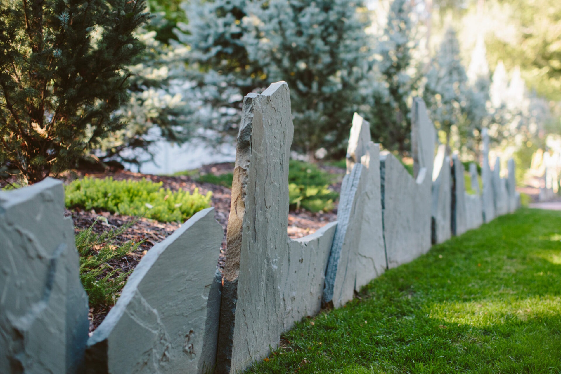 Rough stone slabs form a serrated garden border, surrounded by lush greenery and evergreen trees, creating a natural, serene landscape scene.