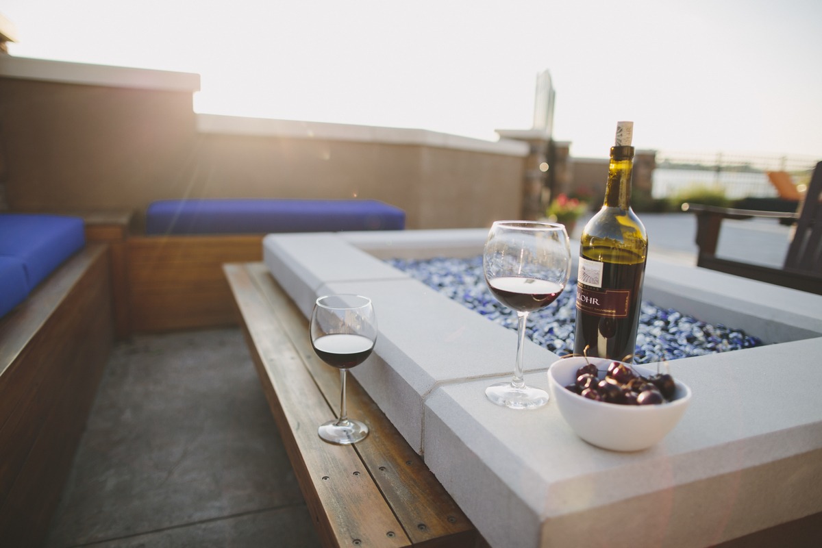 Outdoor setting with two glasses of red wine, a wine bottle, and a bowl of cherries on a wooden table.