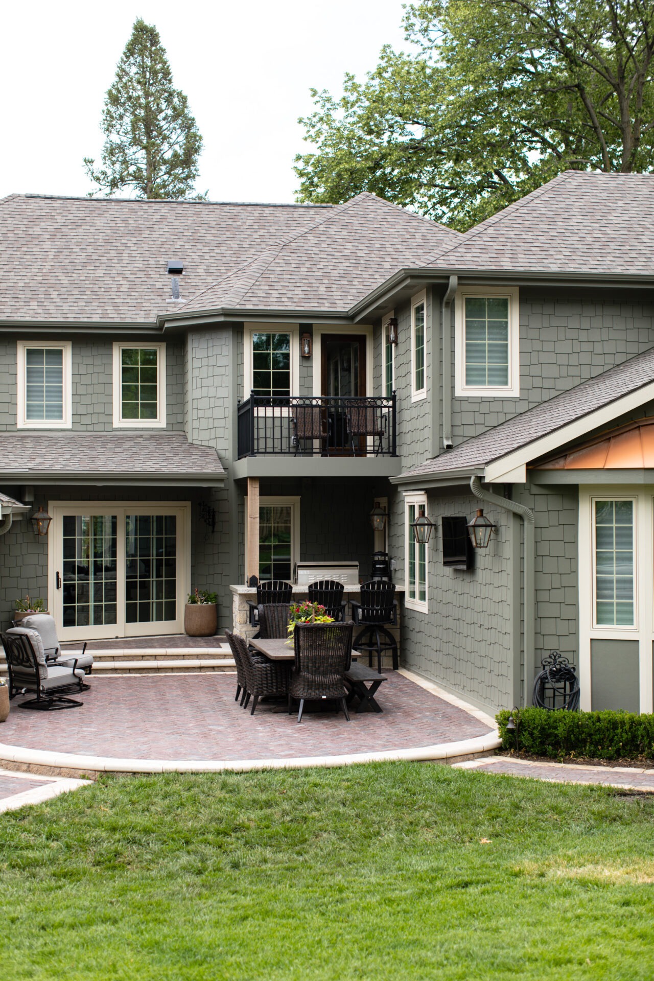 A two-story house with gray shingles, patio furniture, and green lawn. Surrounded by trees, creating a serene and inviting outdoor space.