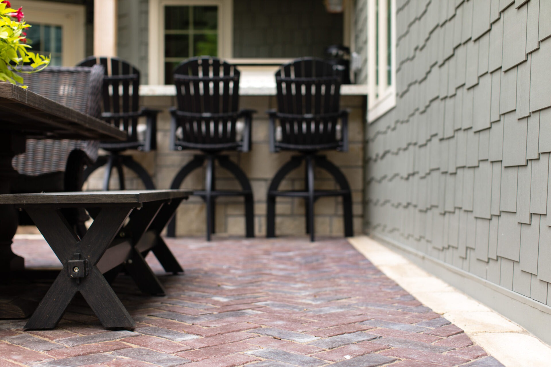 Outdoor patio with black chairs, brick flooring, and green siding. Wooden bench in foreground. Cozy, inviting atmosphere with no people present.