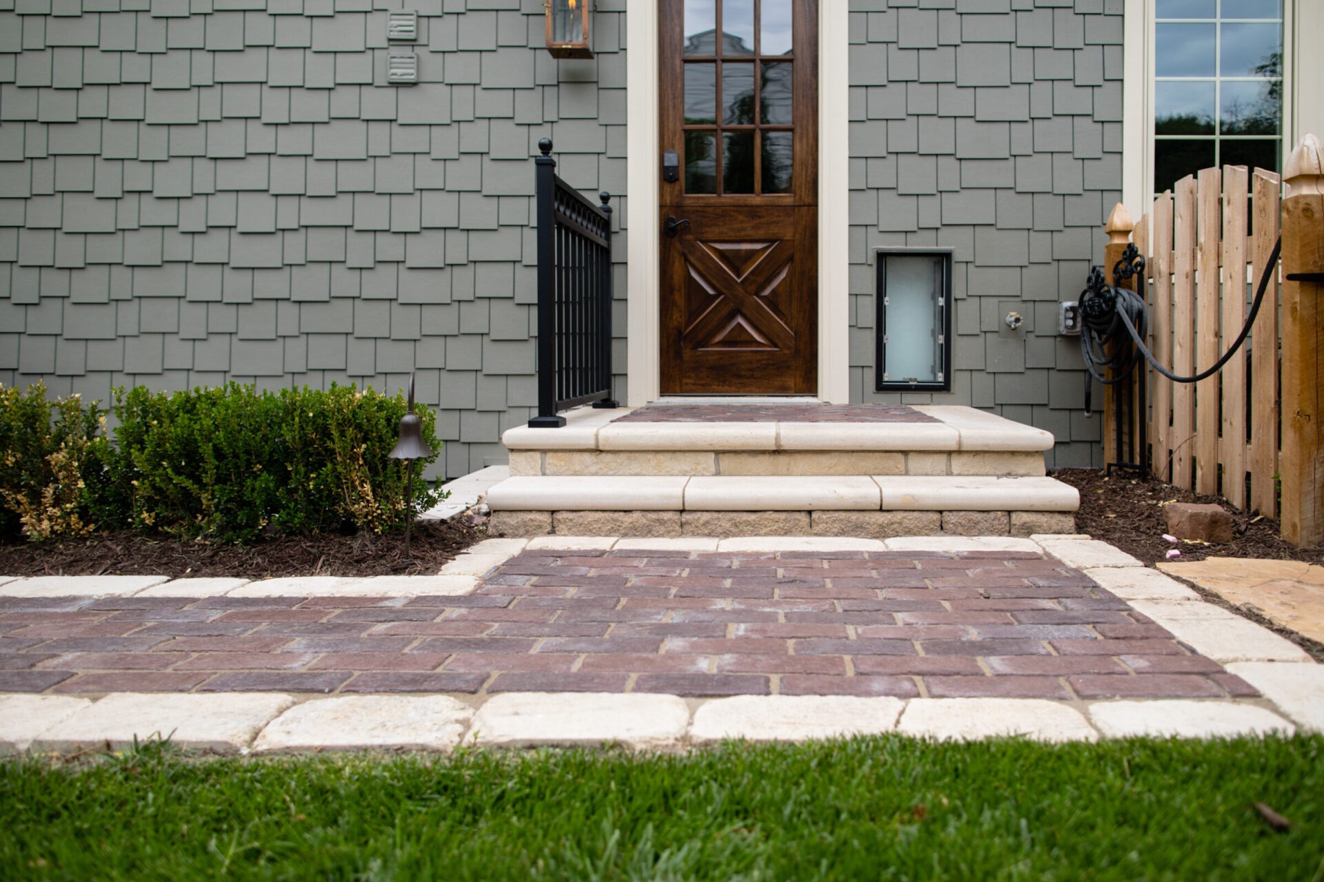 A residential entrance features stone steps, a wooden door, shrubbery, and a small fence, creating a welcoming, tidy pathway to the house.