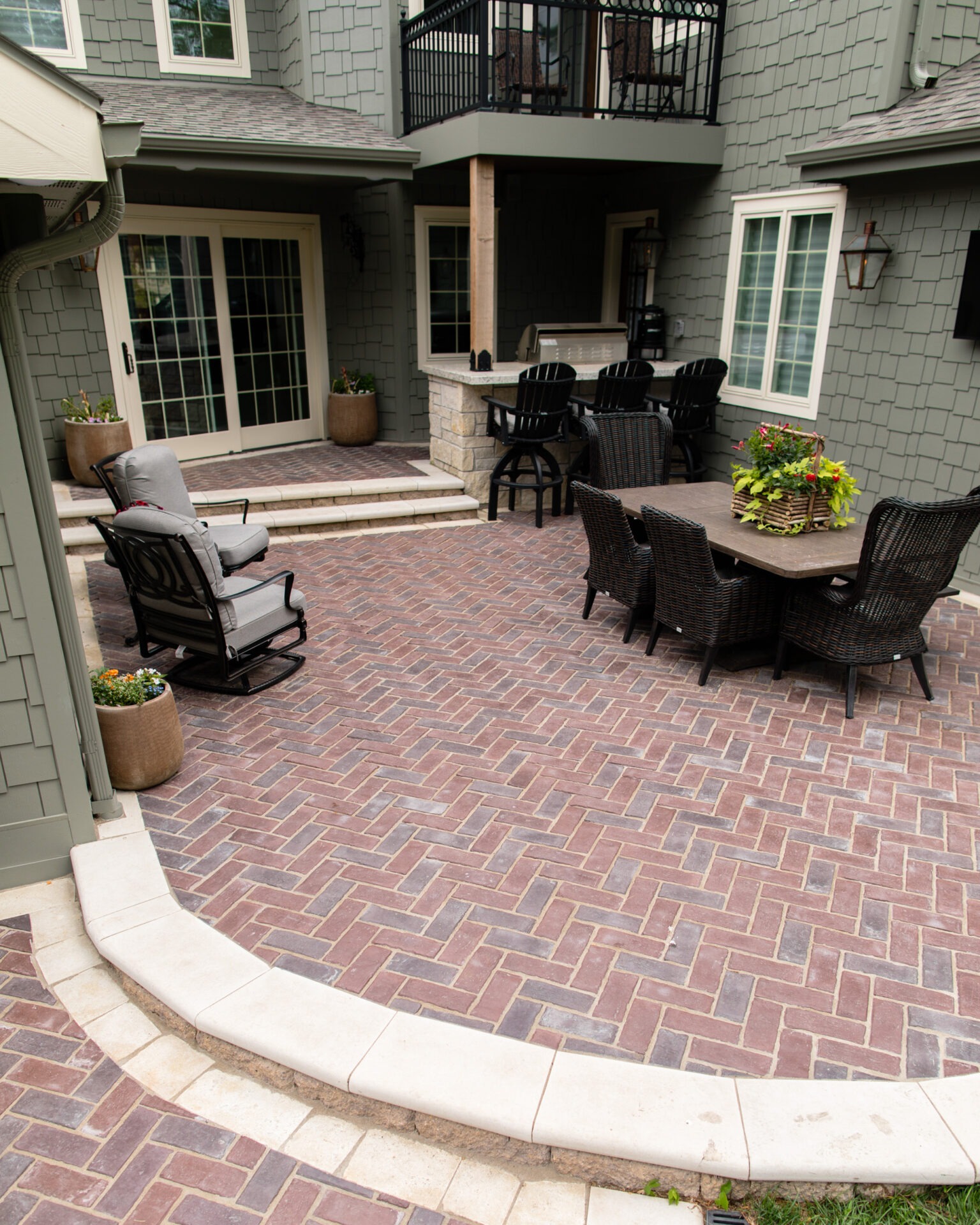 A cozy backyard patio with wicker furniture, brick flooring, and lush potted plants, creating an inviting outdoor living space.