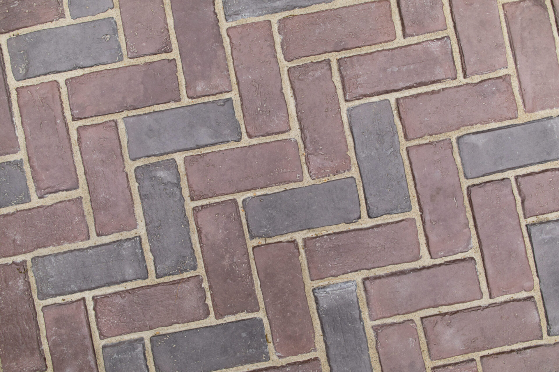 Interlocking brick pattern with varying shades of red and gray, arranged in a herringbone design, forming an intricate and textured mosaic surface.