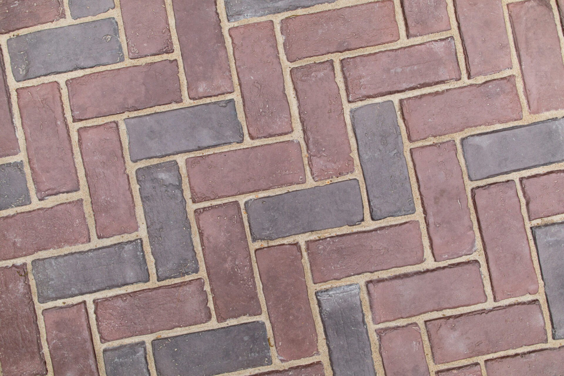 Close-up view of a herringbone-patterned brick pavement, featuring alternating reddish and gray tones, with visible mortar between the bricks.