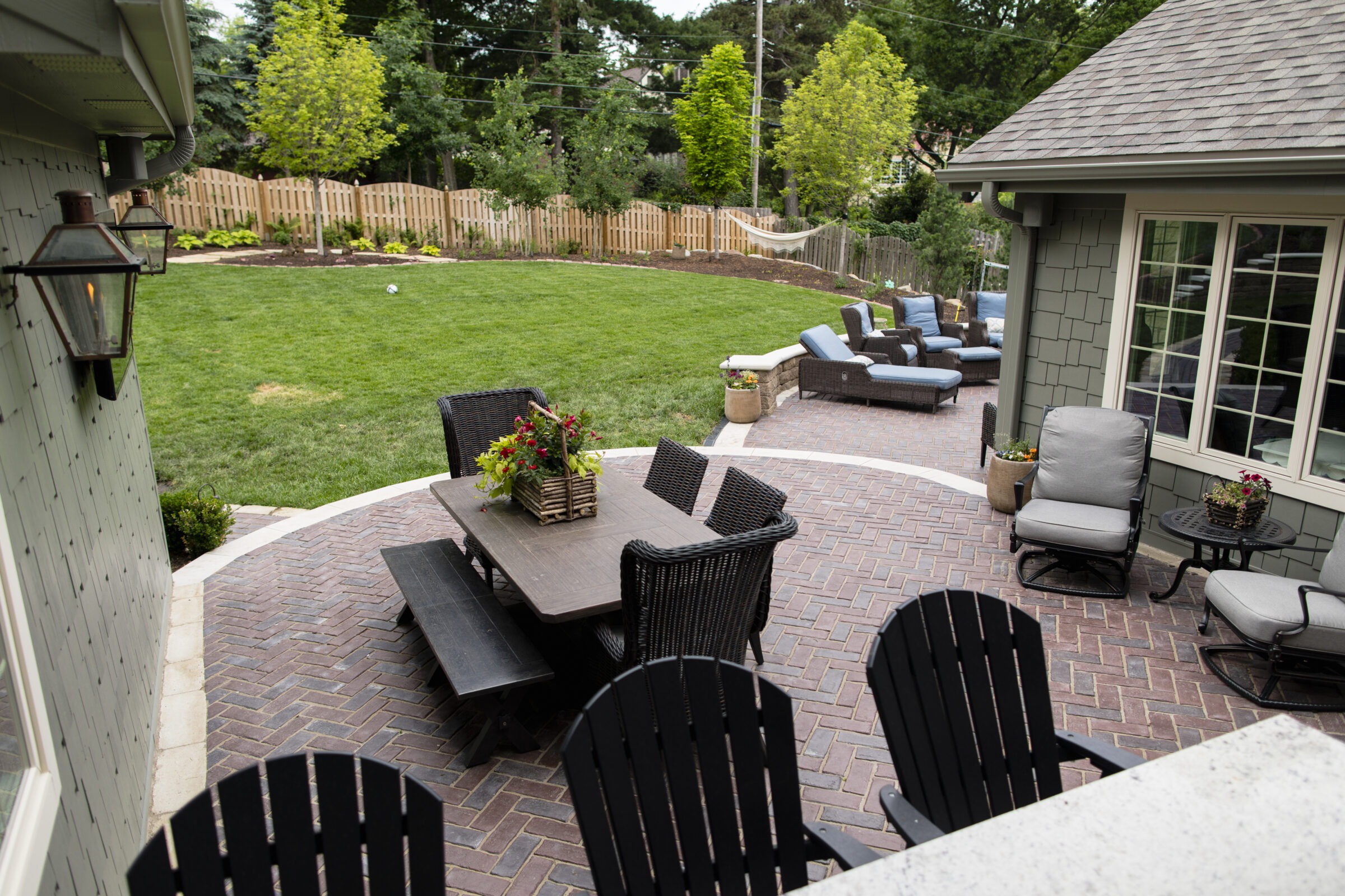 A cozy backyard with patio furniture, a grassy lawn, wooden fence, and hammock, creating a peaceful outdoor living space for relaxation.
