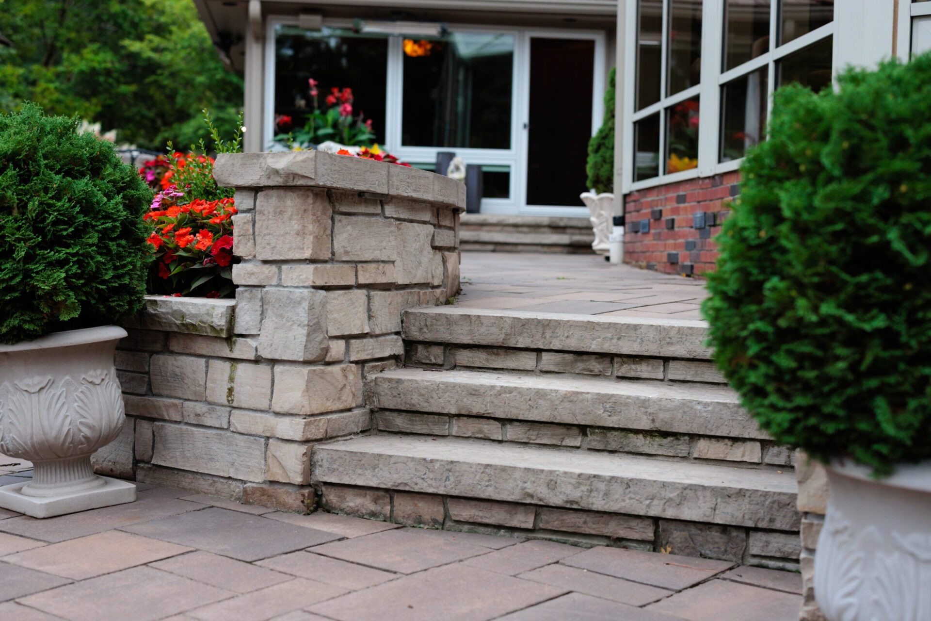 Stone steps lead to a building entrance, surrounded by vibrant flowers and greenery in decorative planters. Peaceful, inviting outdoor setting.