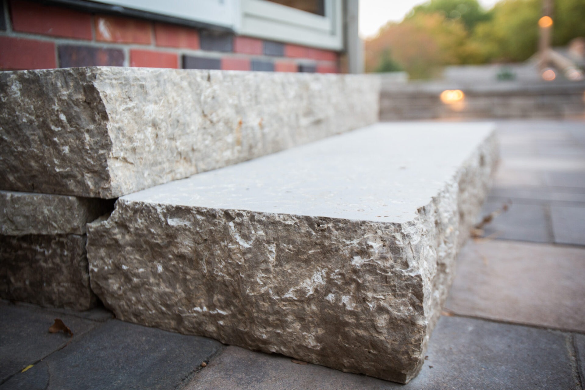 Close-up of stone steps leading to a brick building, with soft background lighting and greenery, creating an inviting outdoor atmosphere.