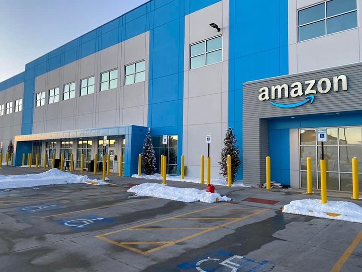 Exterior of an Amazon building with blue accents, snowy surroundings, yellow barriers, and accessible parking spaces in front of the entrance.