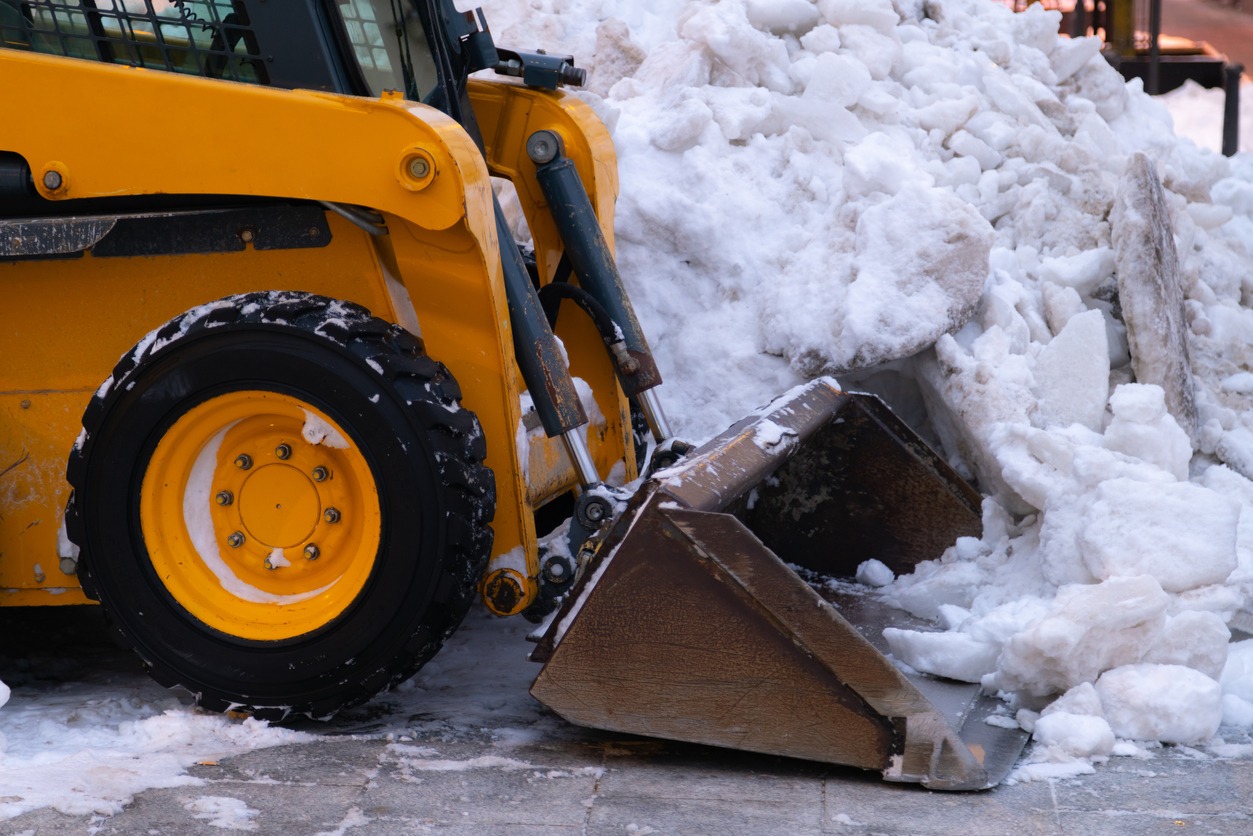 Yellow bulldozer clearing snow on a street. Large pile of snow beside it, showcasing winter cleanup efforts in an urban area.