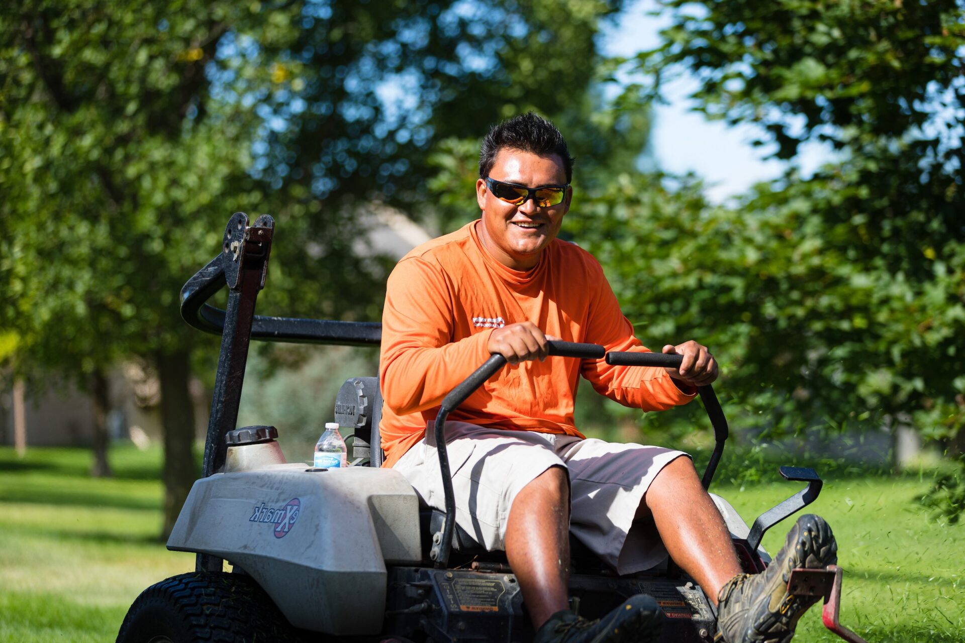 A Sun Valley team member on a riding mower on a sunny day with trees in the background.