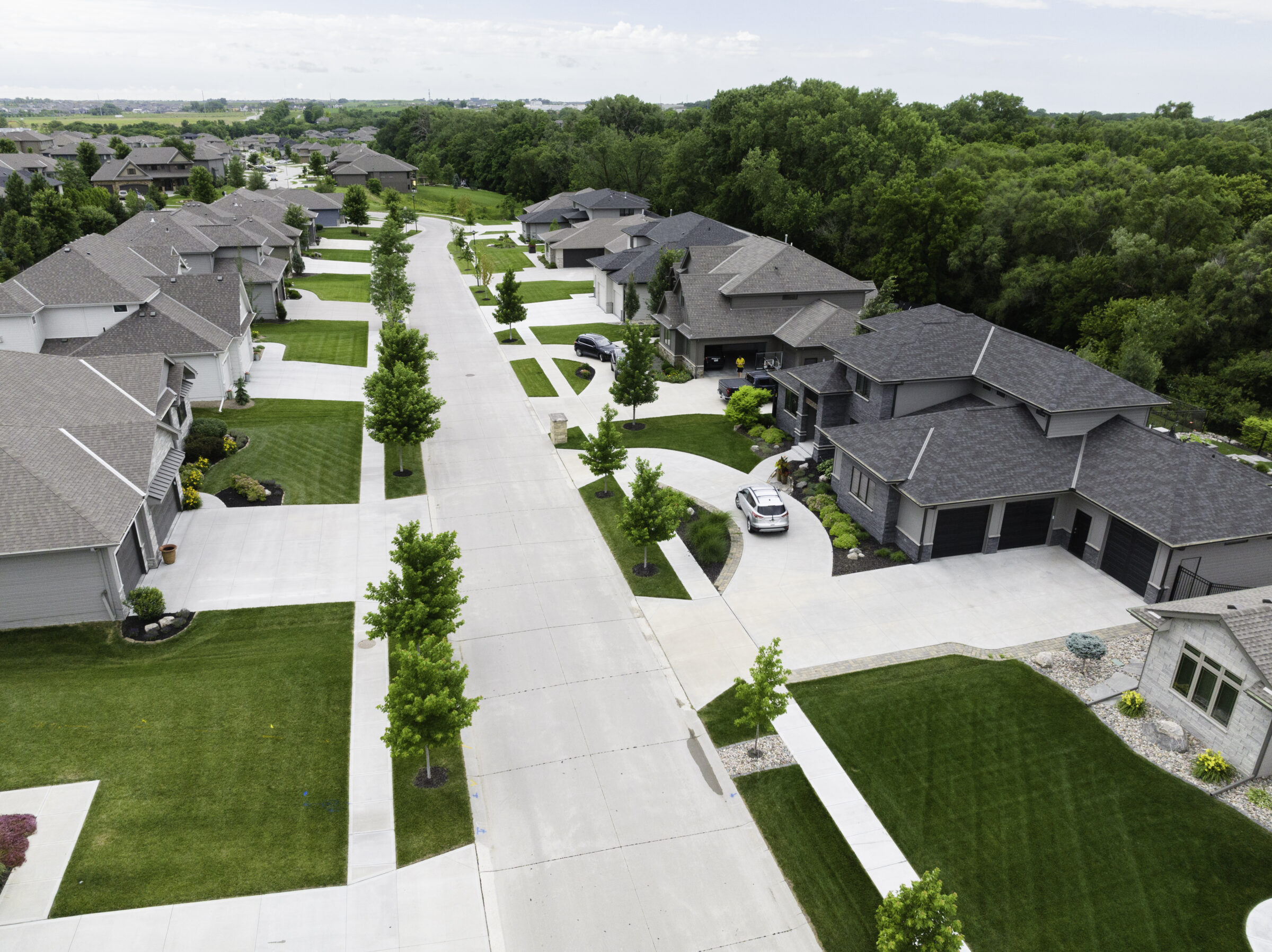 Aerial view of a suburban neighborhood with neatly mowed lawns, trees along sidewalks, and modern homes.