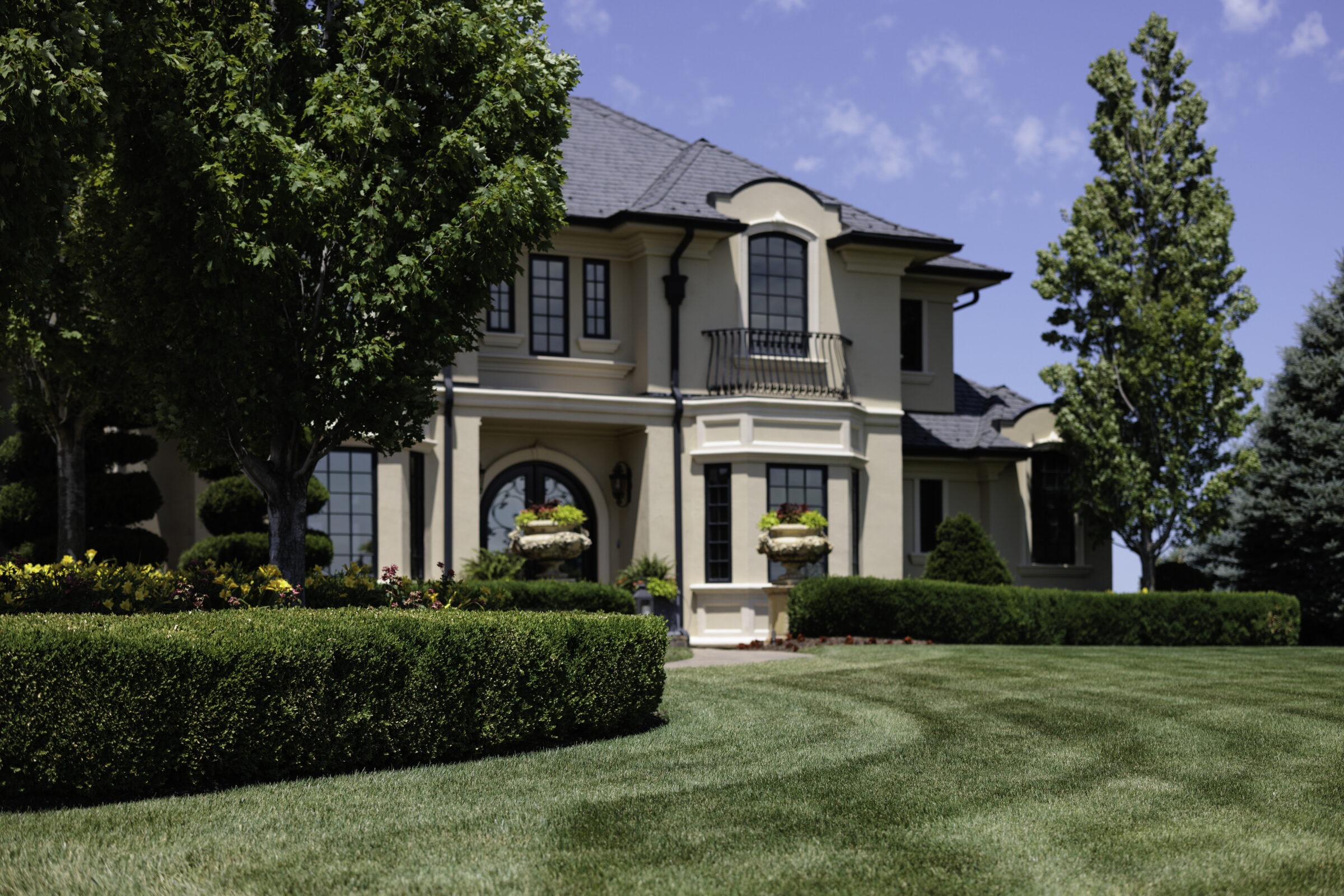 Elegant front yard with manicured hedges and large home.