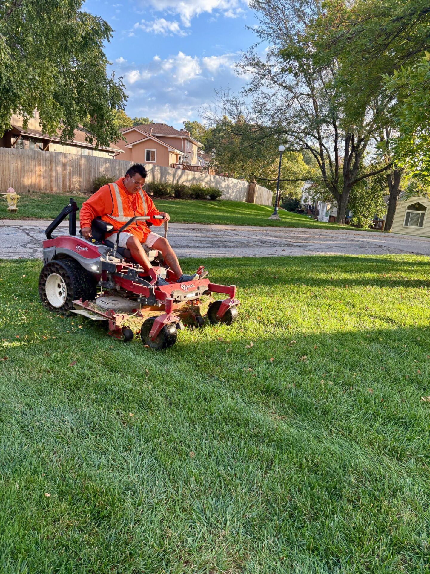 Landscaper on mower cutting residential lawn under blue sky.