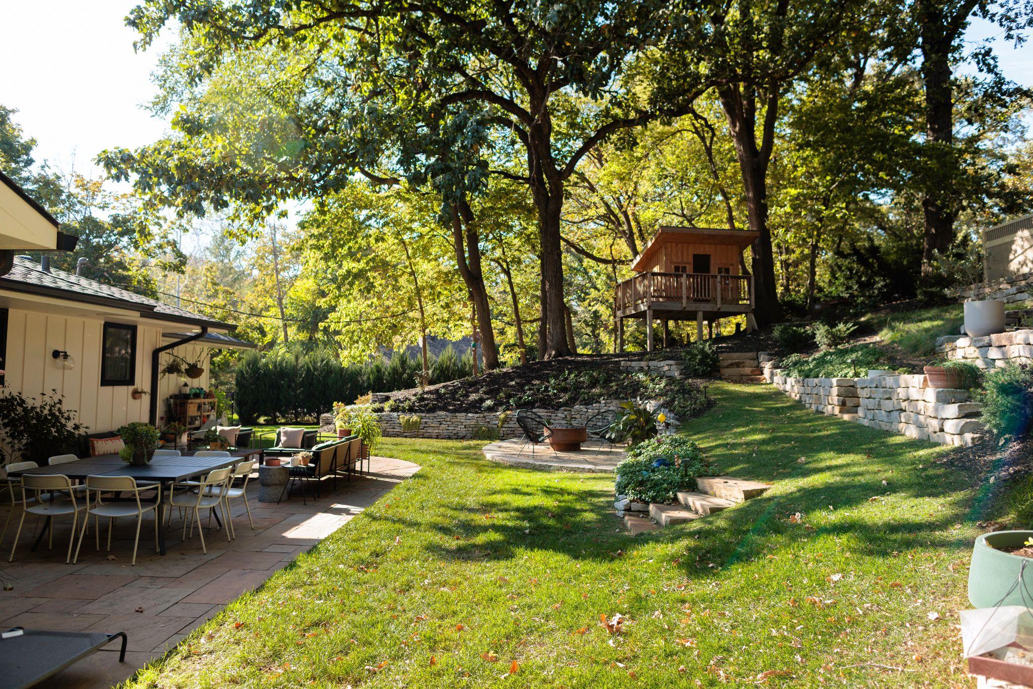 Spacious backyard with treehouse, stone walls, and outdoor seating area.