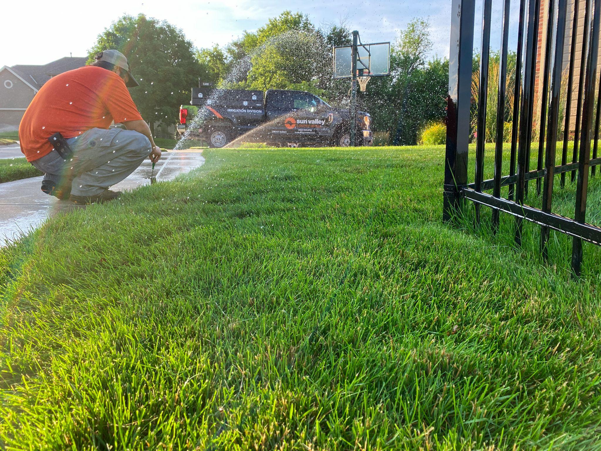 Technician adjusting sprinkler head on lush green lawn.