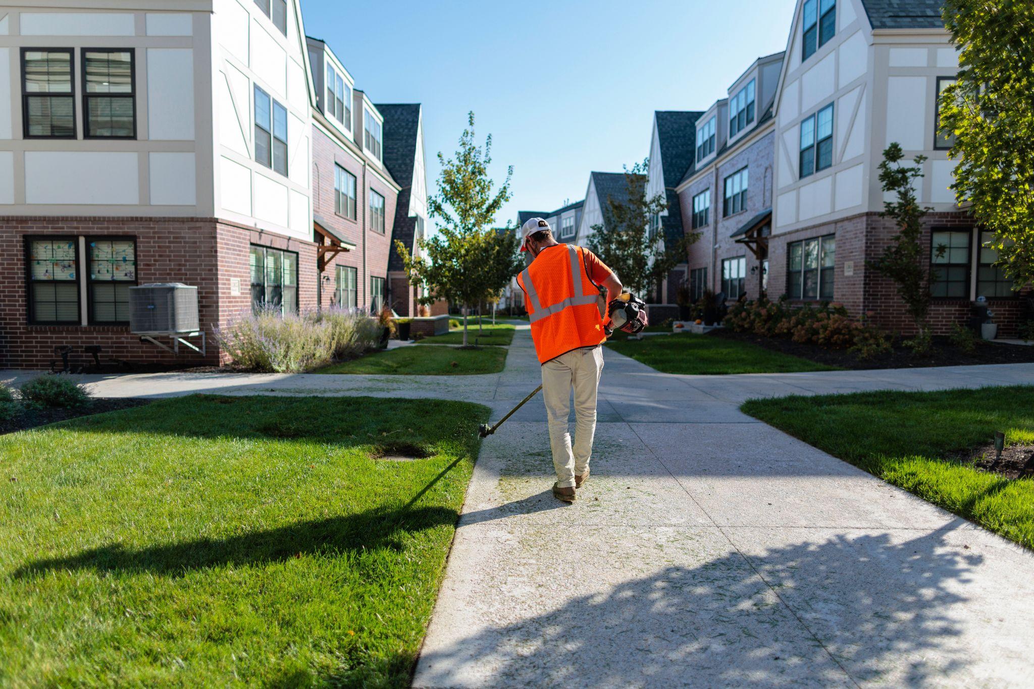 Worker edging sidewalk in a well-maintained apartment complex lawn.