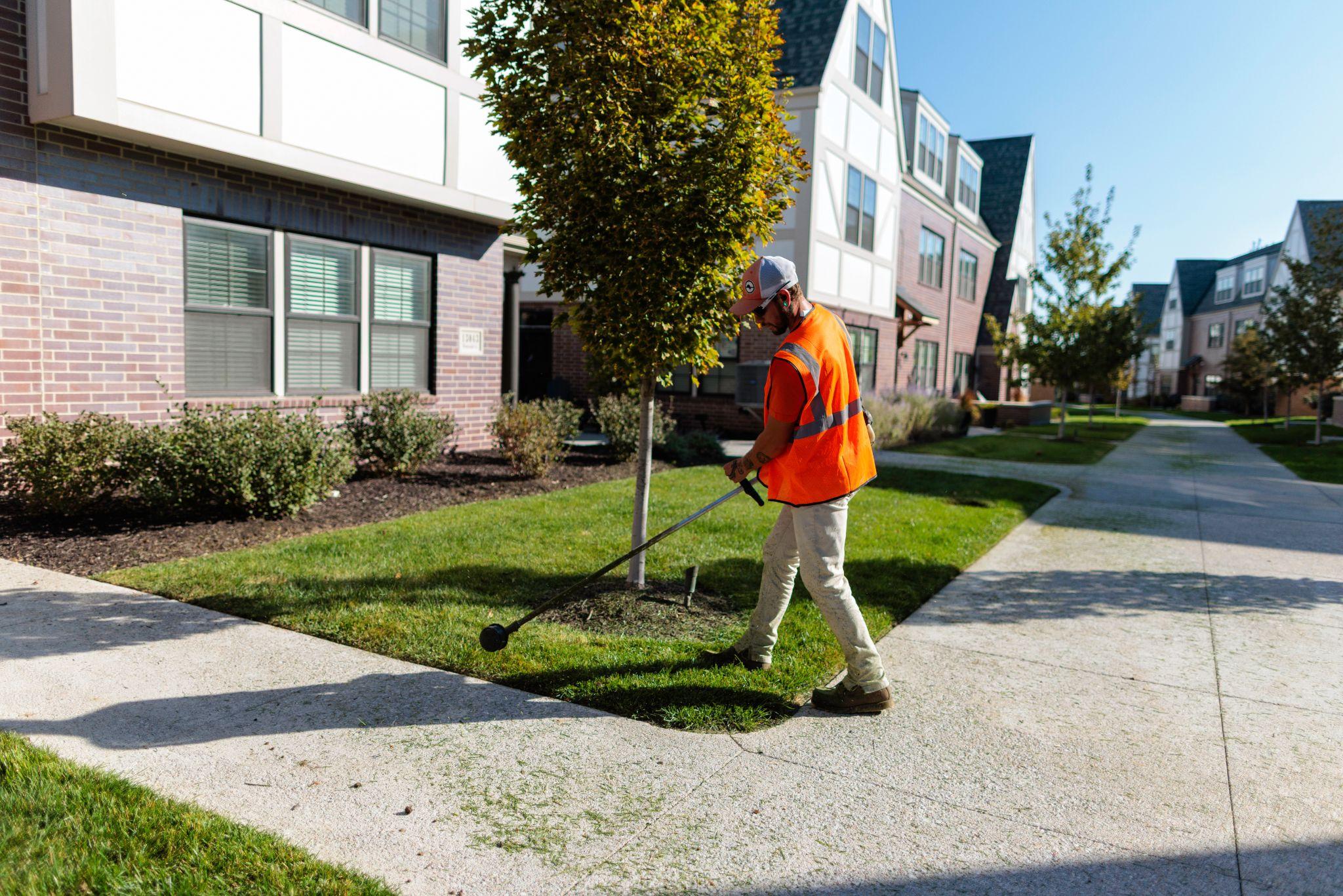 Worker edging turf near a tree in a residential complex.